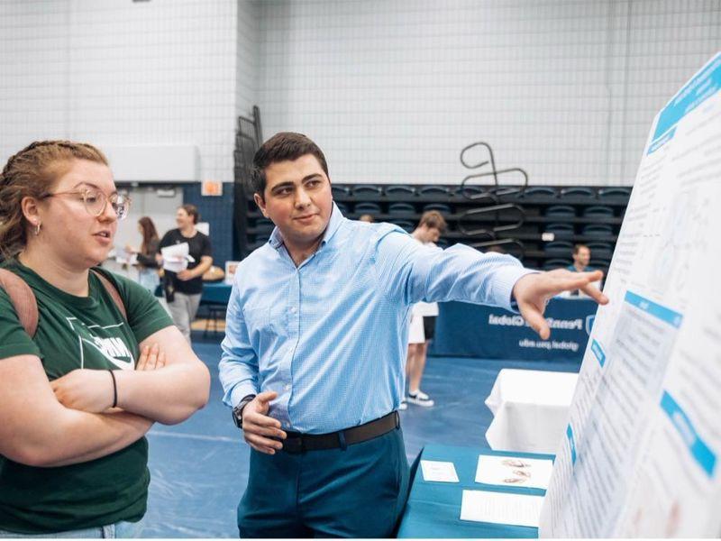 A student points to his research poster board, explaining its contents to an interested visitor.